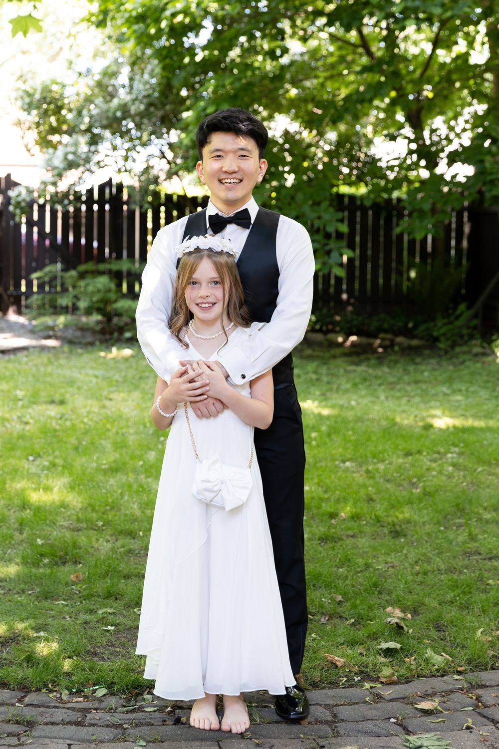 Groom in suit stands with niece surrounded by greenery on the morning of the london, ontario wedding.