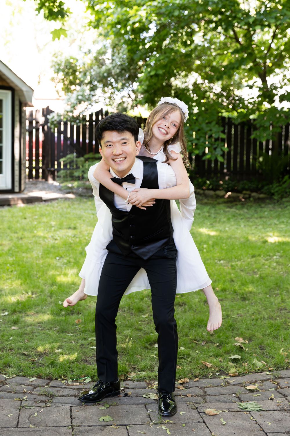Groom in suit gives niece in white dress a piggy back in the backyard of their home on the morning of their london, ontario wedding.