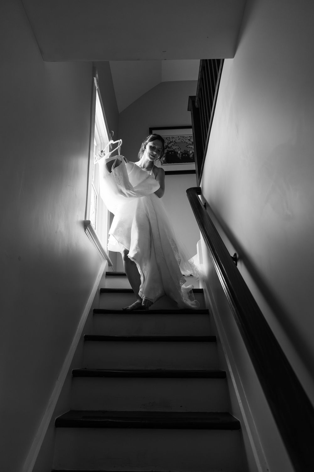 Black and white photo of a bride in a flowing wedding dress descending a staircase, holding her veil during a london, ontario wedding.