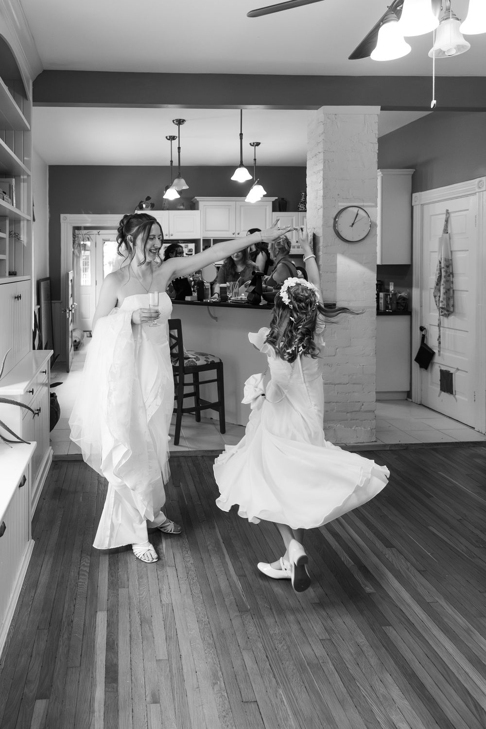 Bride in white gown twirling flower girl in kitchen during wedding day preparations, black and white photo, in a london, ontario wedding.