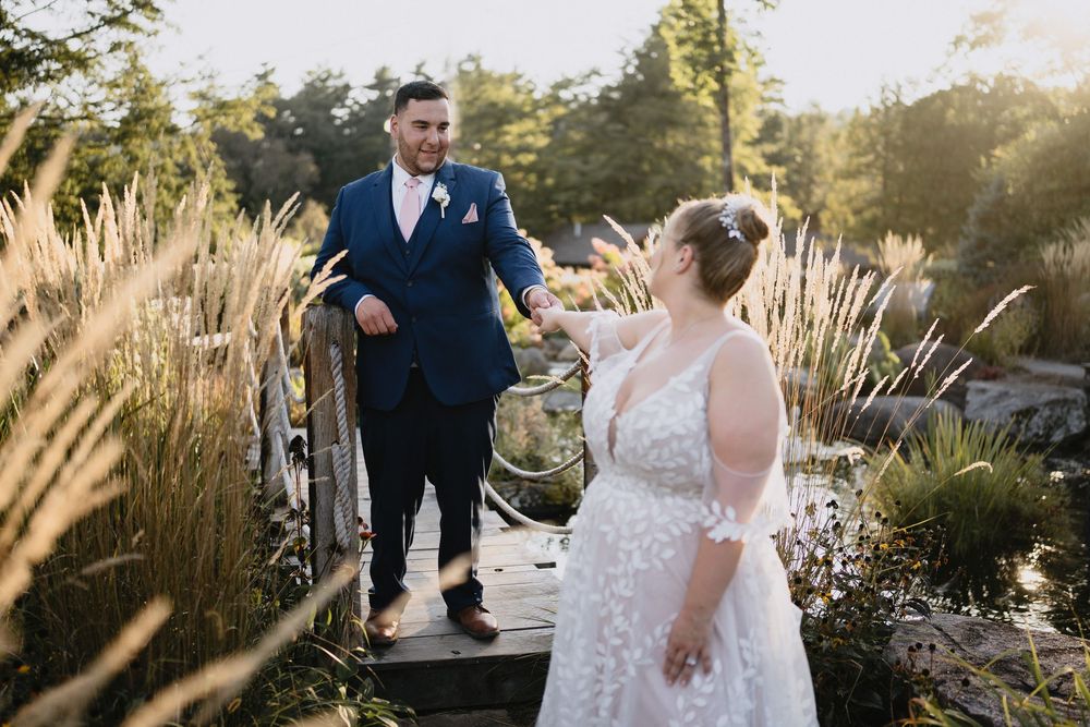 Bride and groom hold hands on a wooden bridge surrounded by tall grasses during a golden hour outdoor wedding.