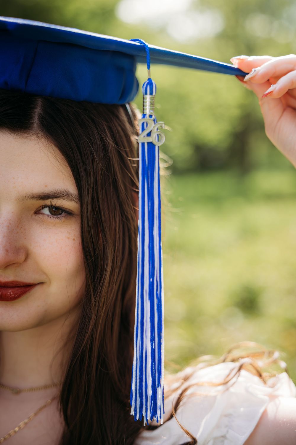 Young woman wearing a blue graduation cap with tassel outdoors, celebrating academic achievement.