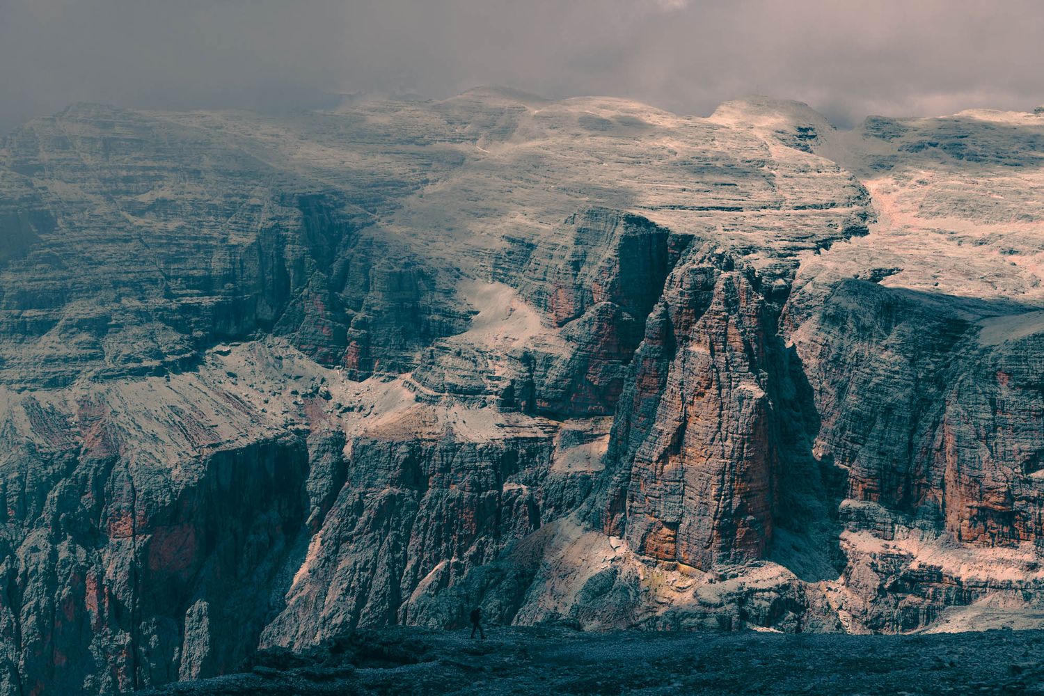 Dramatic Dolomite mountains with jagged rocky peaks, winding road, and moody overcast sky in the Italian Alps.