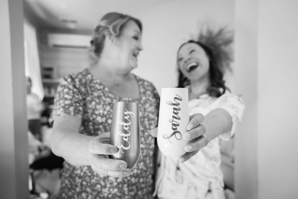 Black and white photo of two women laughing while holding personalized wedding day drink cans.