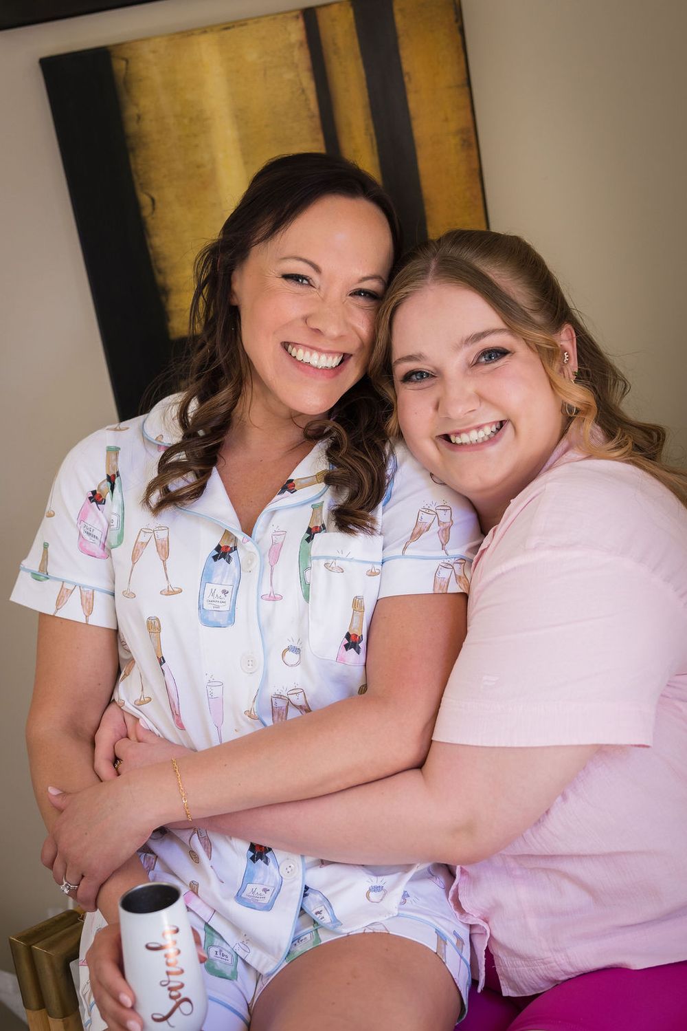 Two women in pajamas smiling and hugging during a bridal getting-ready party.