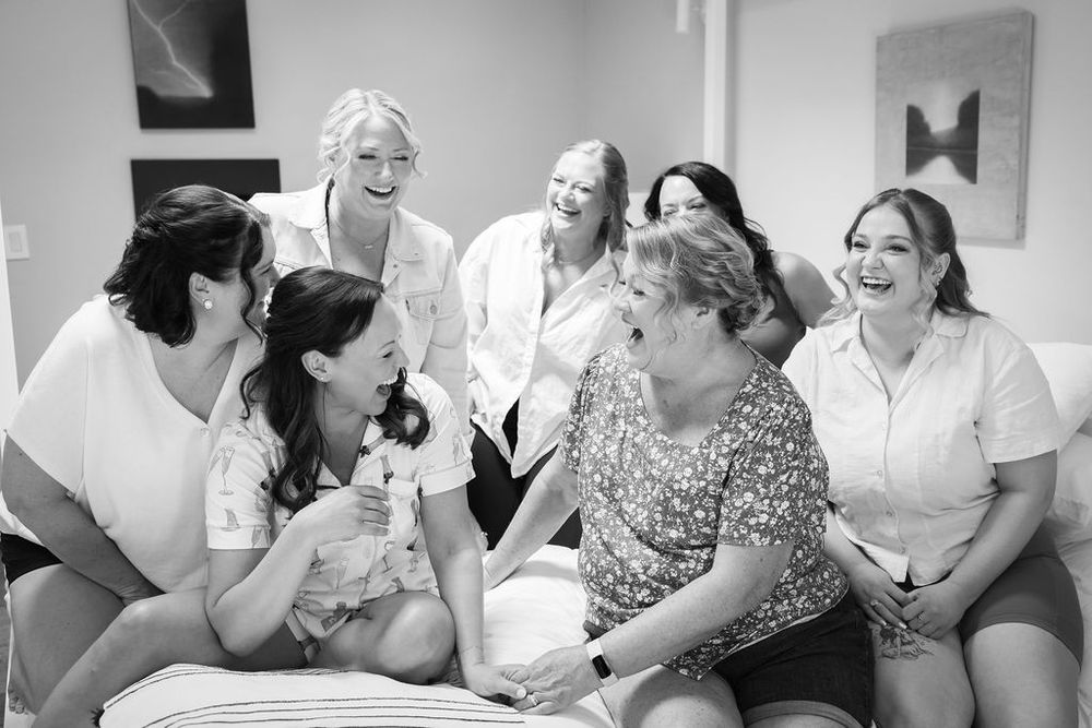 Bridesmaids laughing and sharing joyful moments with the bride during wedding preparations in a bright room.