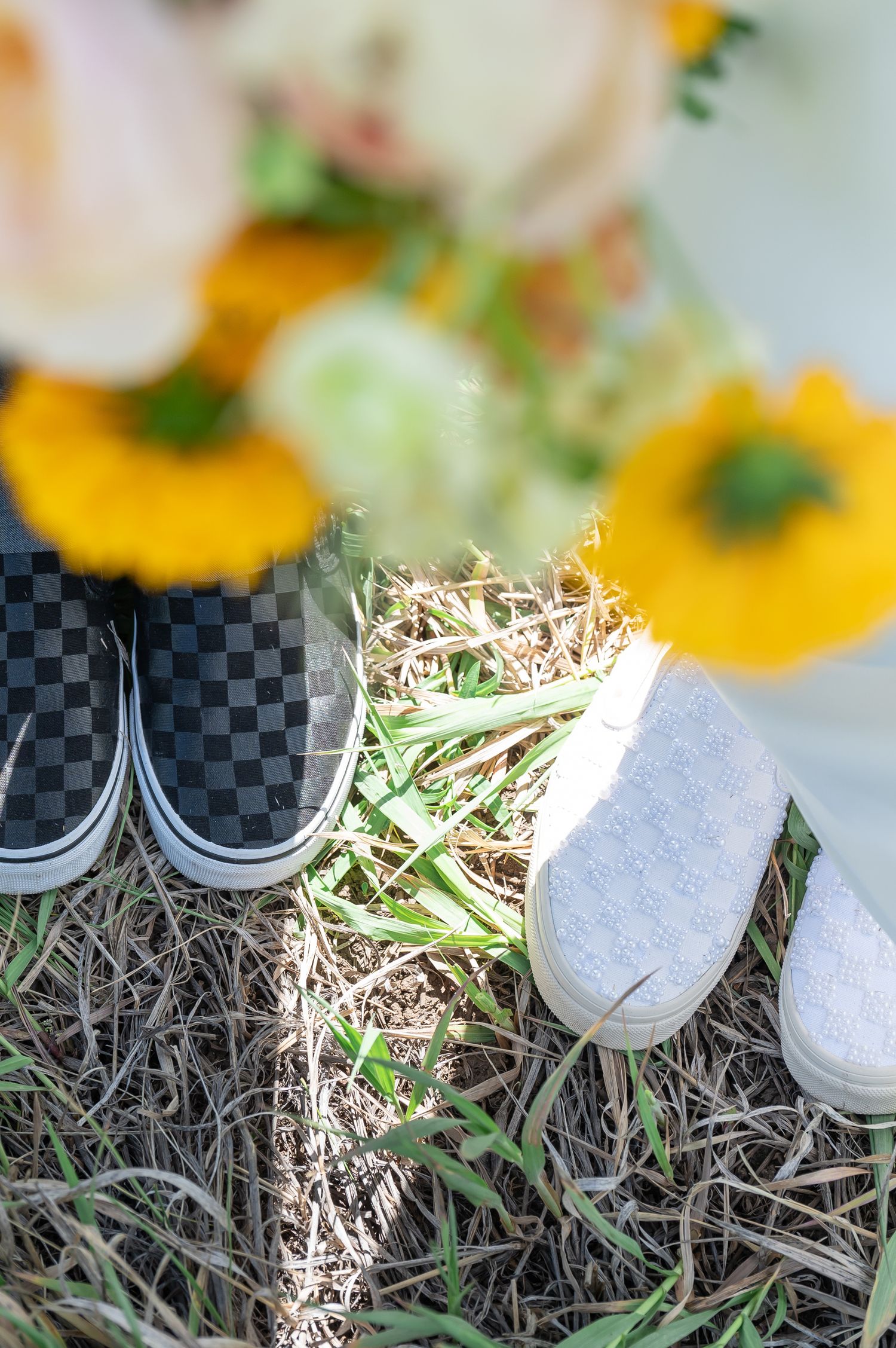 Checkered Vans and gray slip-on shoes rest on grass beside a colorful yellow and white wedding bouquet for Vail elopement
