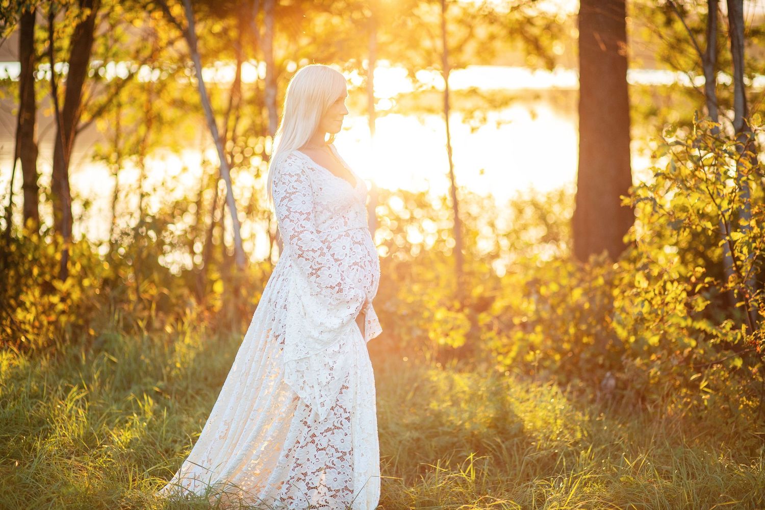 A maternity portrait features a burgundy dress against evergreen trees in winter.