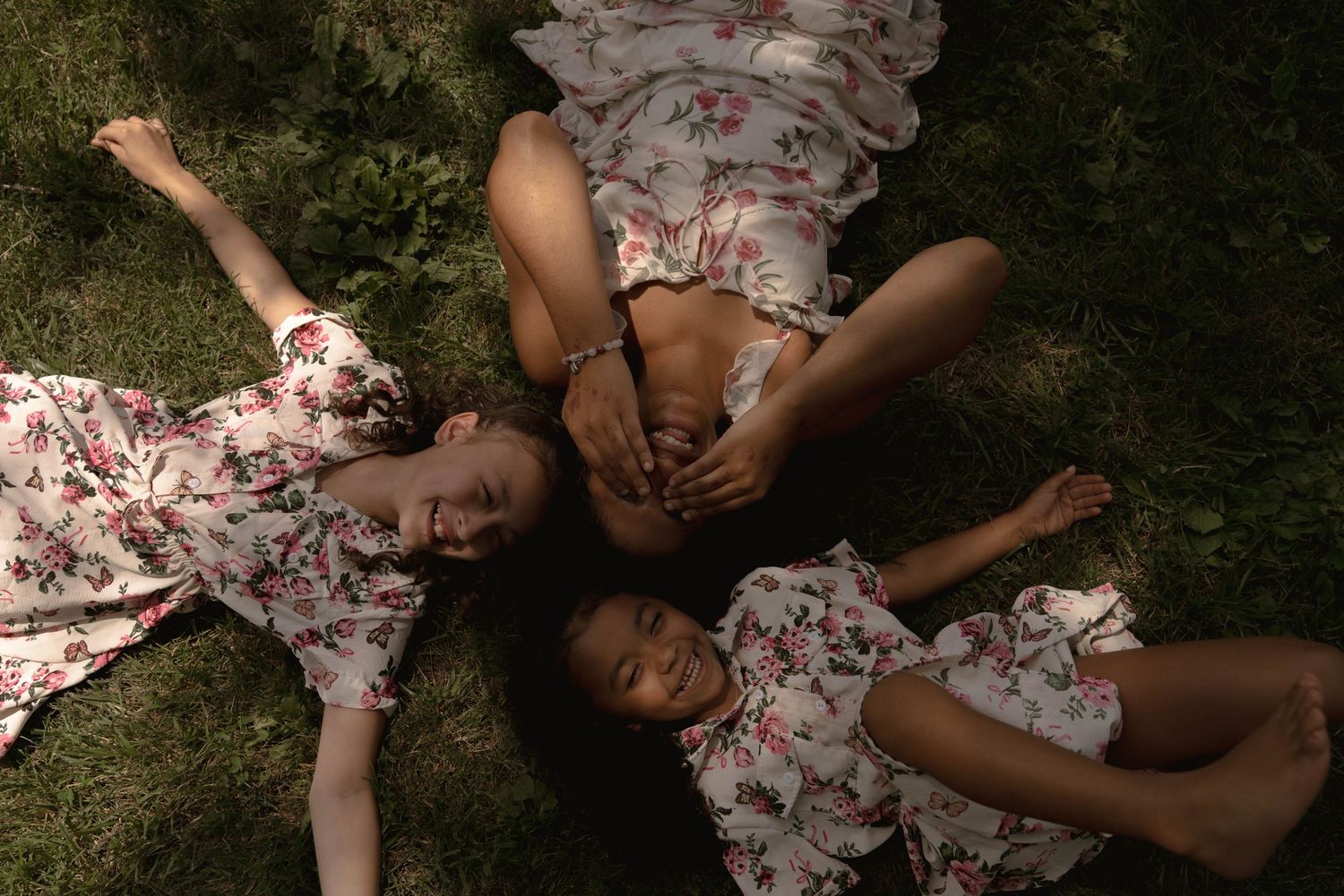 A person in a floral dress relaxes on grass during an outdoor photoshoot.