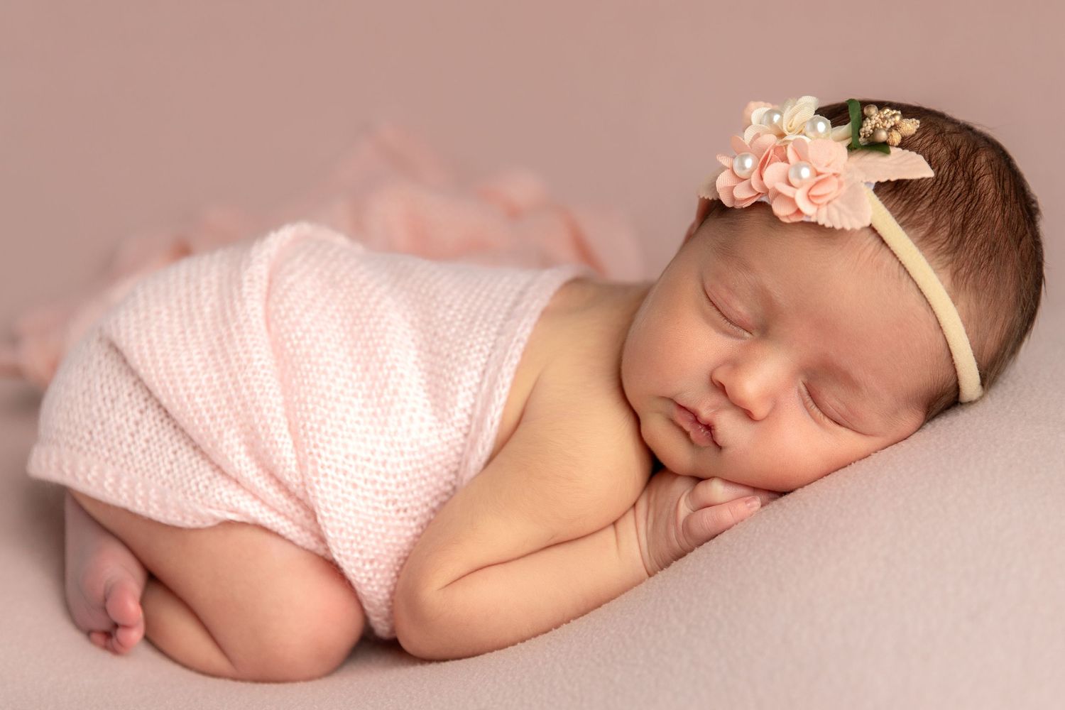 Newborn posed on tummy in soft pastel pinks wrap and backdrop during proessional photography session Dubai