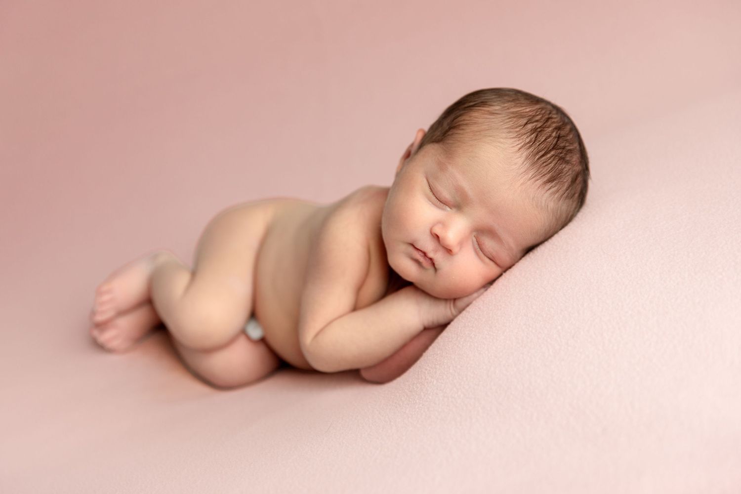 Artistic posed newborn portrait with soft pink backdrop in Dubai