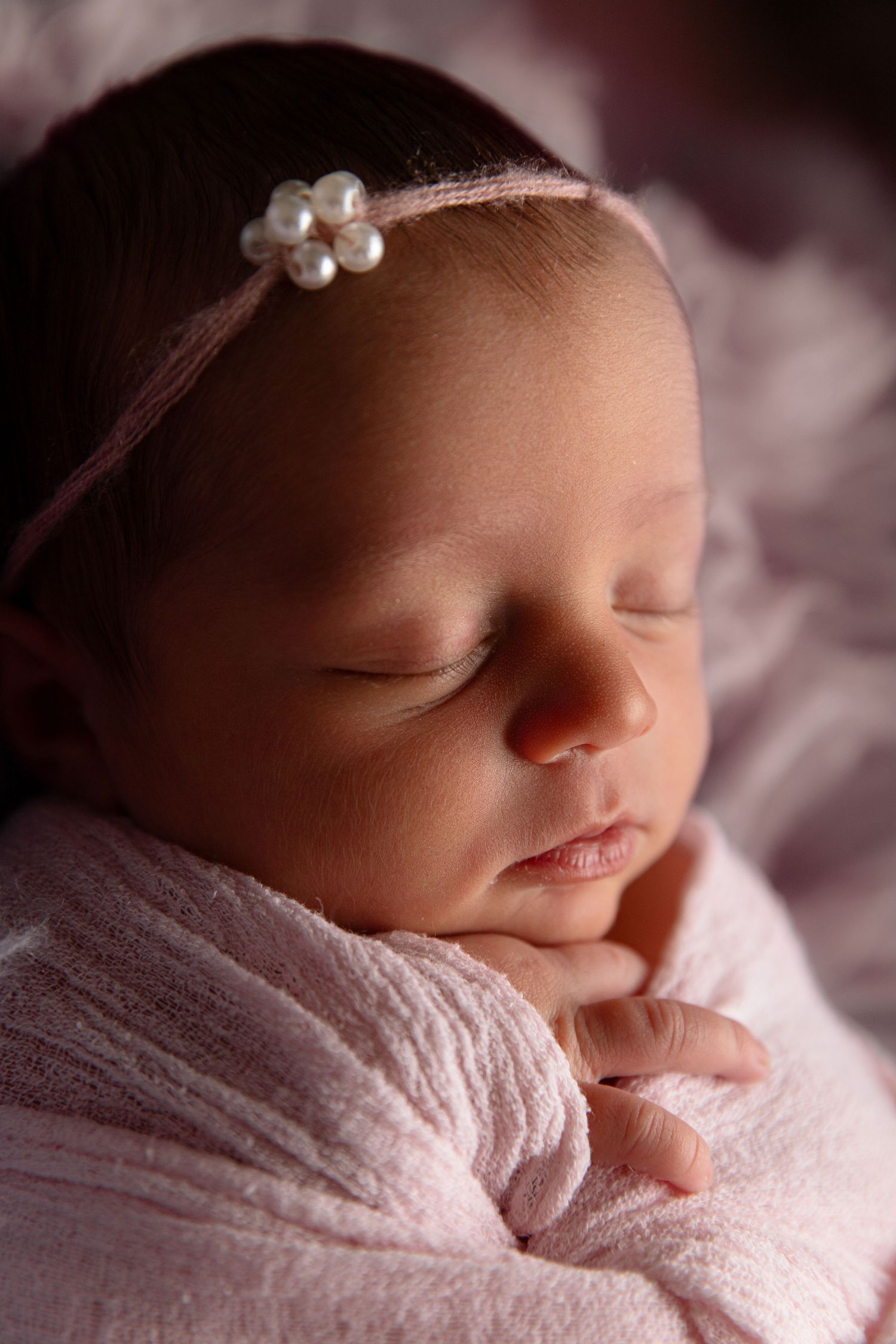 Classic posed newborn photo with baby swaddled in soft pink wrap on textured backdrop