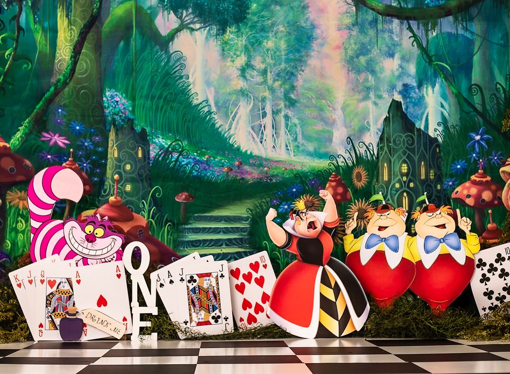 Whimsical Alice in Wonderland themed mural featuring playing cards, teacups, and fantasy forest elements on a long wall.