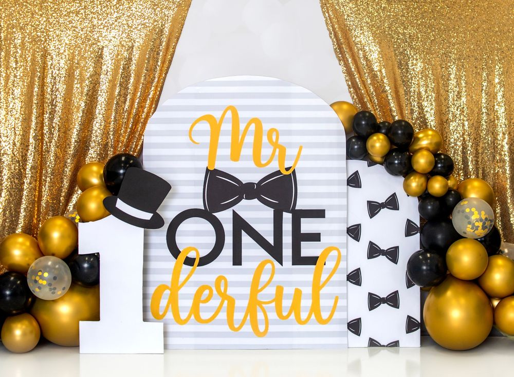 Gold and black holiday party decorations with bow ties and ornaments against a sparkly gold backdrop.
