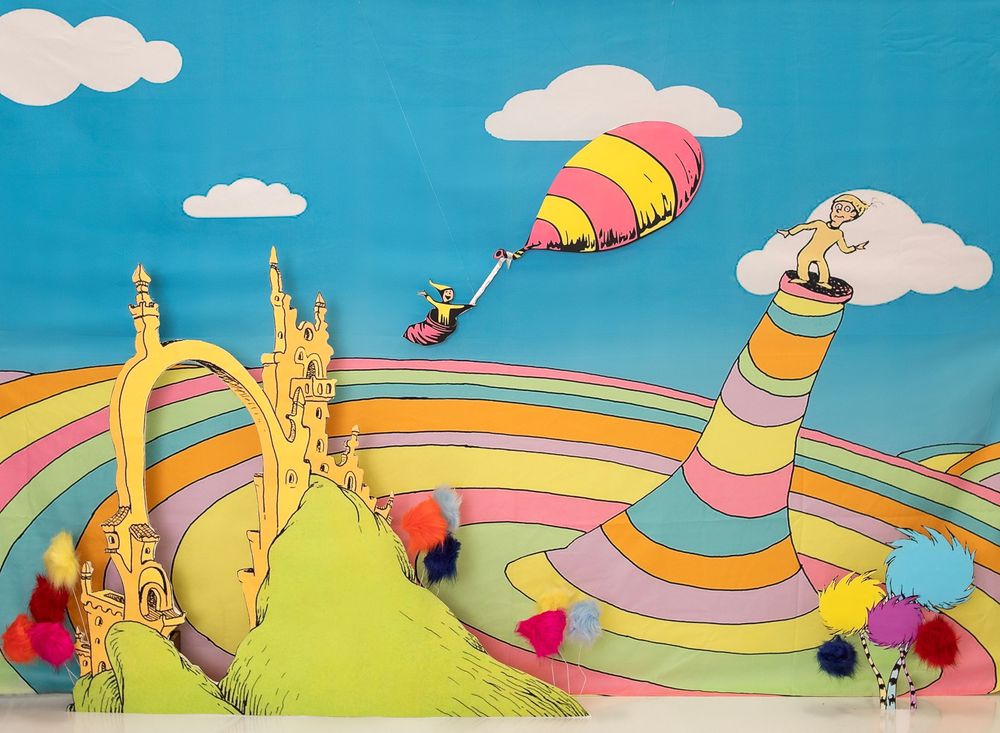 A whimsical illustration of a rainbow road winding through a bright landscape with clouds and flying figures.