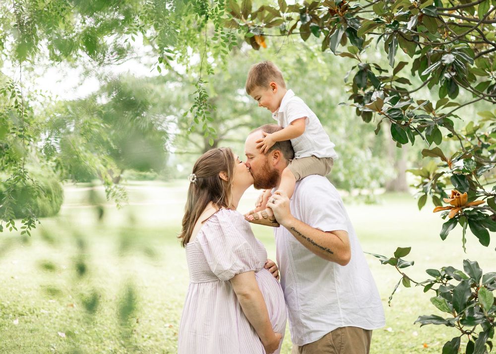 A tender family moment captured under blooming trees in a sunlit garden.