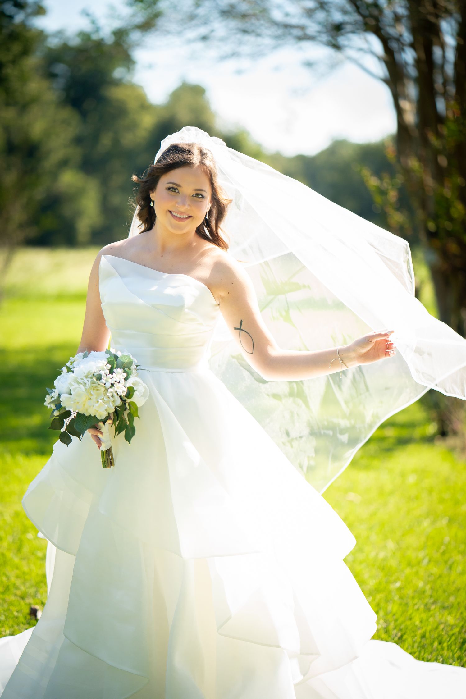 A flowing white wedding dress billows gracefully in the sunlight as the wearer stands in a lush green meadow.