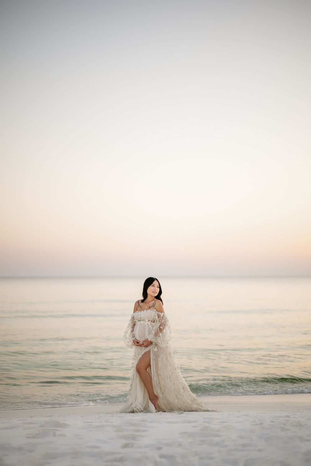A romantic beach wedding scene at sunset with a couple sitting on white sand as gentle waves roll in.