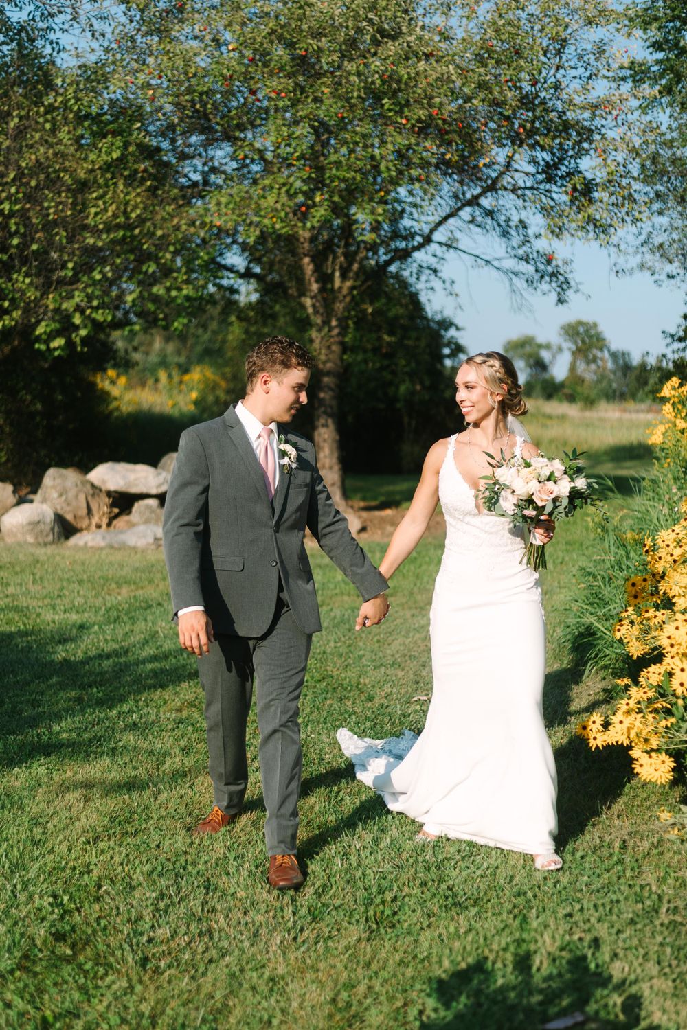 Newlyweds walk hand in hand through a lush garden setting on their wedding day.