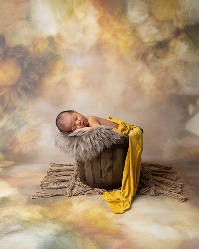 A sleeping newborn wrapped in yellow fabric lies on a rustic wooden backdrop with dreamy lighting and soft textures.