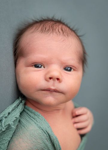 A baby wearing a soft mint green wrap gazes at the camera in a series of close-up portraits against a gray background.