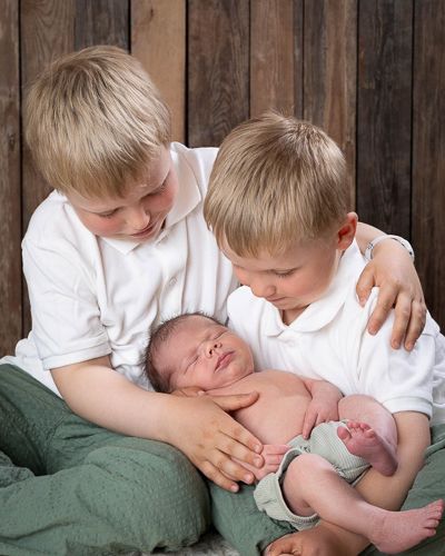 A series of five heartwarming photos showing siblings gently kissing and embracing a newborn baby on a blanket.