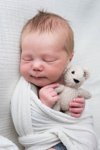 A sleeping newborn baby swaddled in white fabric cuddles with a small knitted toy.