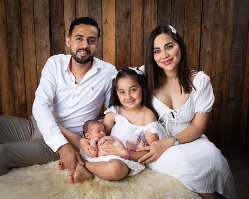 A series of family photos in white outfits against a rustic wooden wall background showing parents with their newborn baby.