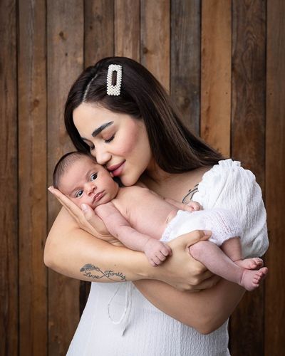 A tender moment between mother and newborn baby against a rustic wooden wall background.