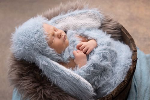 Baby med blå kanindrakt liggende i en trebolle på brun bakgrunn. Nyfødtfotografering i studio på Fjerdingby på Romerike
