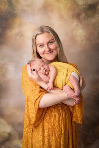 En mor i gul kjole holder sin nyfødte baby.Nyfødtfotografering i studio på Fjerdingby på Romerike
