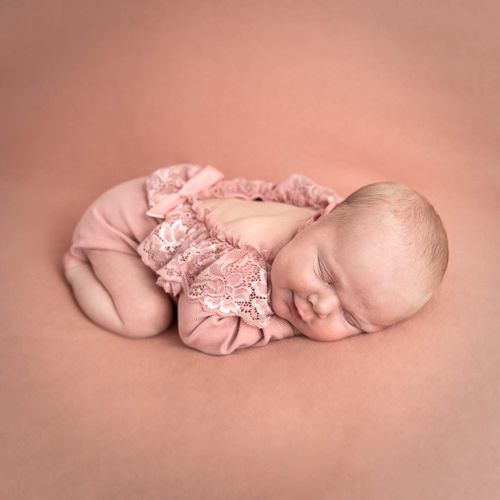 Nyfødt baby sovende på rosa teppe. Hun har på et rosa antrekk med blonder. Nyfødtfotografering i studio på Fjerdingby på Romerike