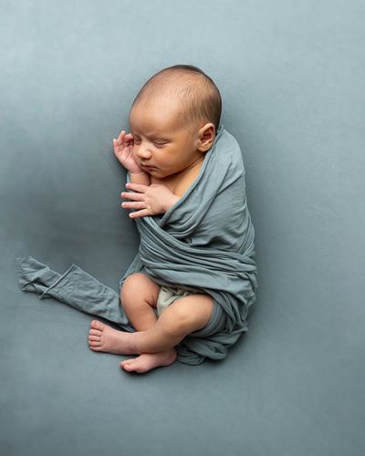 Sovende nyfødt baby svøpt i grønt klede på grønt teppe.Nyfødtfotografering i studio på Fjerdingby på Romerike