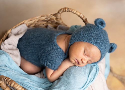 A sleeping newborn baby wearing a blue knit hat rests peacefully on light blue blankets.
