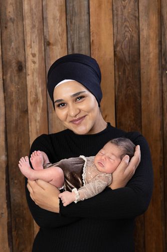 Three heartwarming photos of a woman in a hijab cradling and bonding with a sleeping newborn baby against a wooden backdrop.