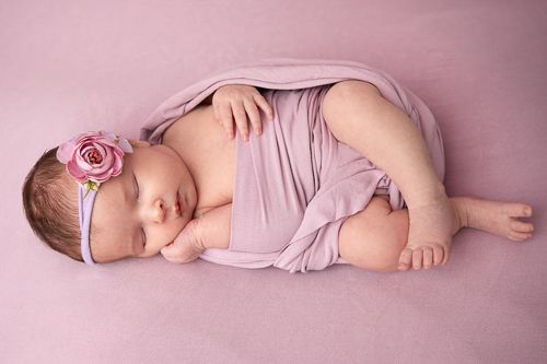 Sovende baby med rosa klede på rosa teppe med blomsterhårbånd.Nyfødtfotografering i studio på Fjerdingby på Romerike