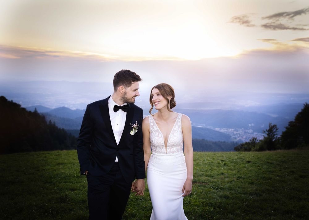 Sunset mountain wedding portrait with couple in formal attire against misty valley view.