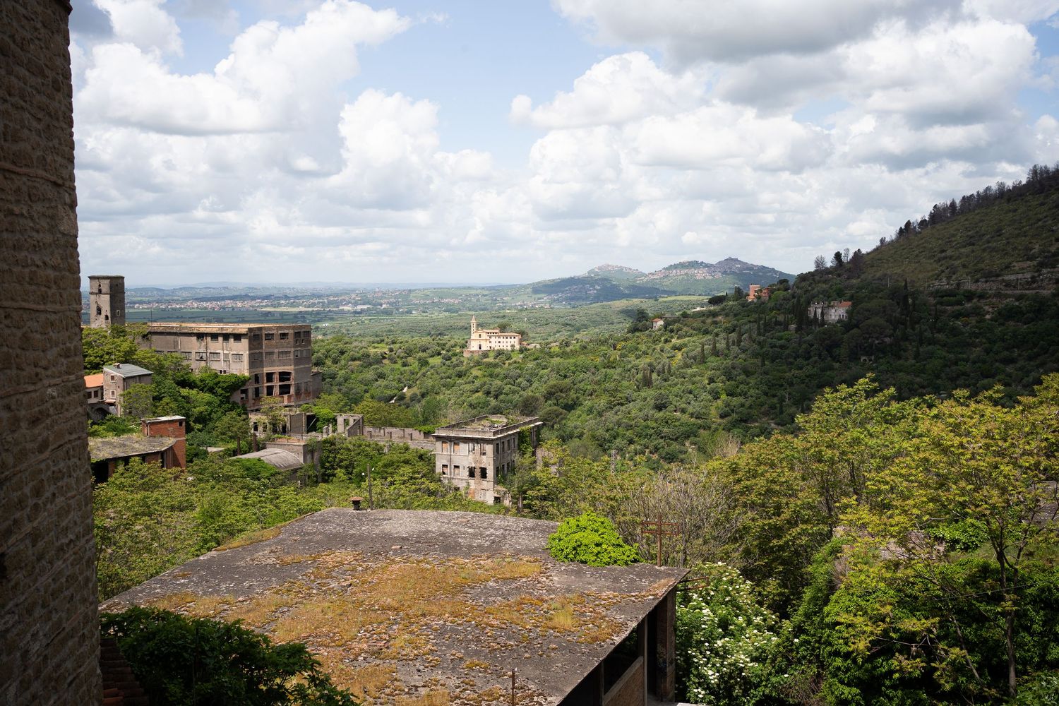 Scenic panoramic view of rolling Tuscan hills with stone buildings and cypress trees dotting the verdant landscape.