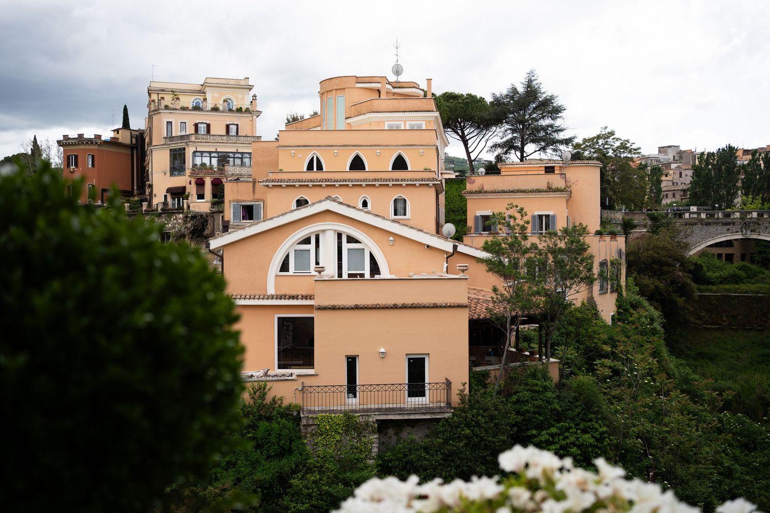 Historic Mediterranean style buildings with terracotta roofs nestled among lush trees on a hillside.