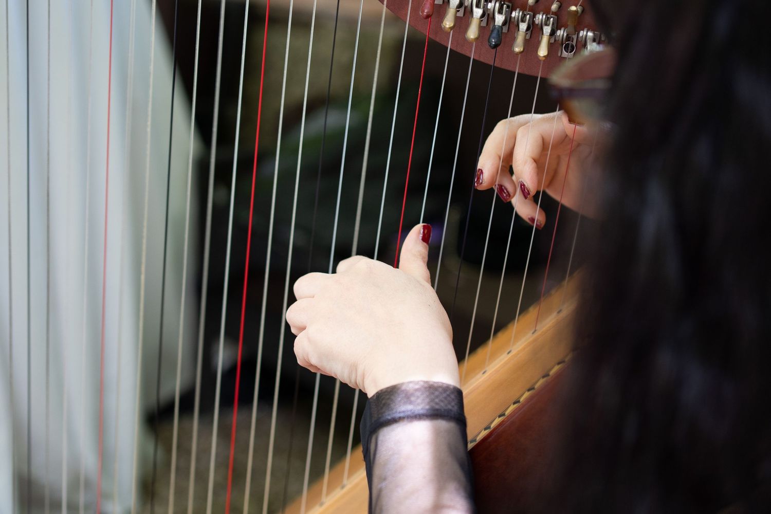 Close-up view of hands playing a golden orchestral harp with ornate details and strings.