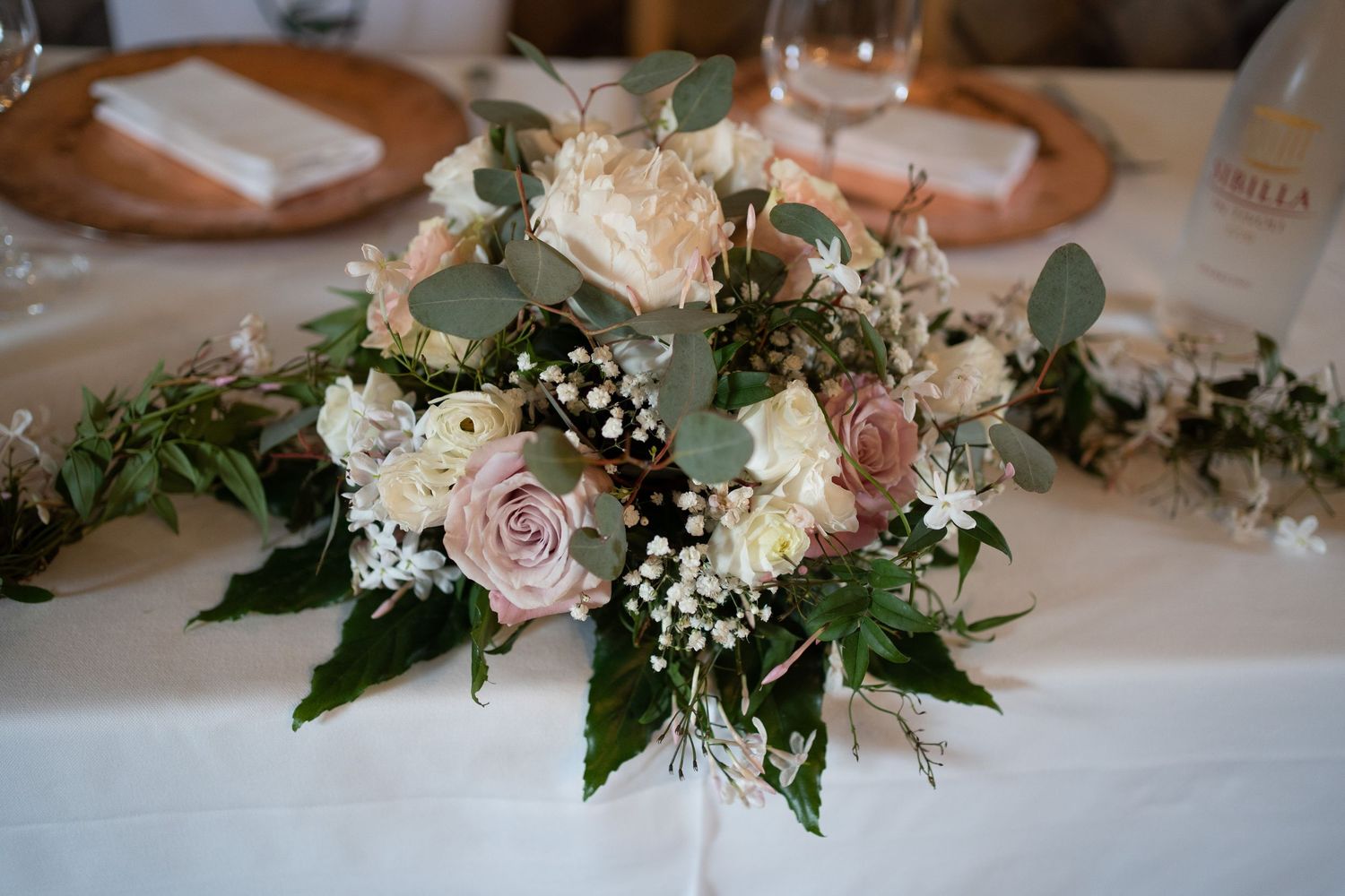 Delicate pink and white floral centerpiece arrangements with roses and greenery displayed on a white tablecloth.