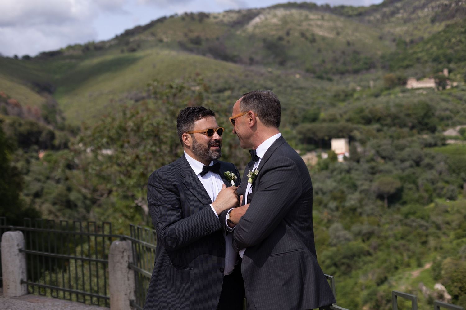 Two people share a romantic moment against a backdrop of rolling green hills and mountains.