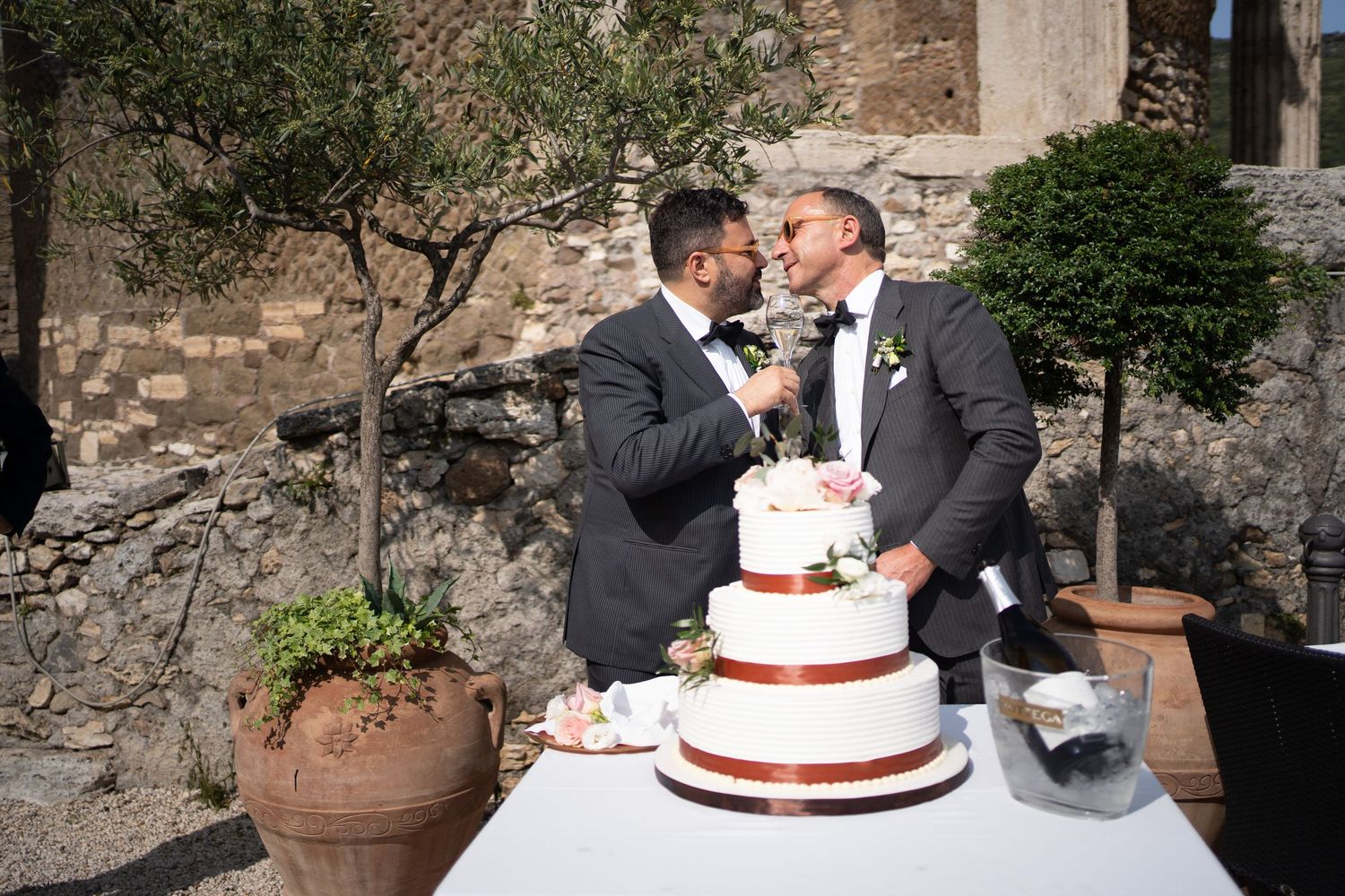 A couple cuts their white and red wedding cake together at an outdoor stone venue.