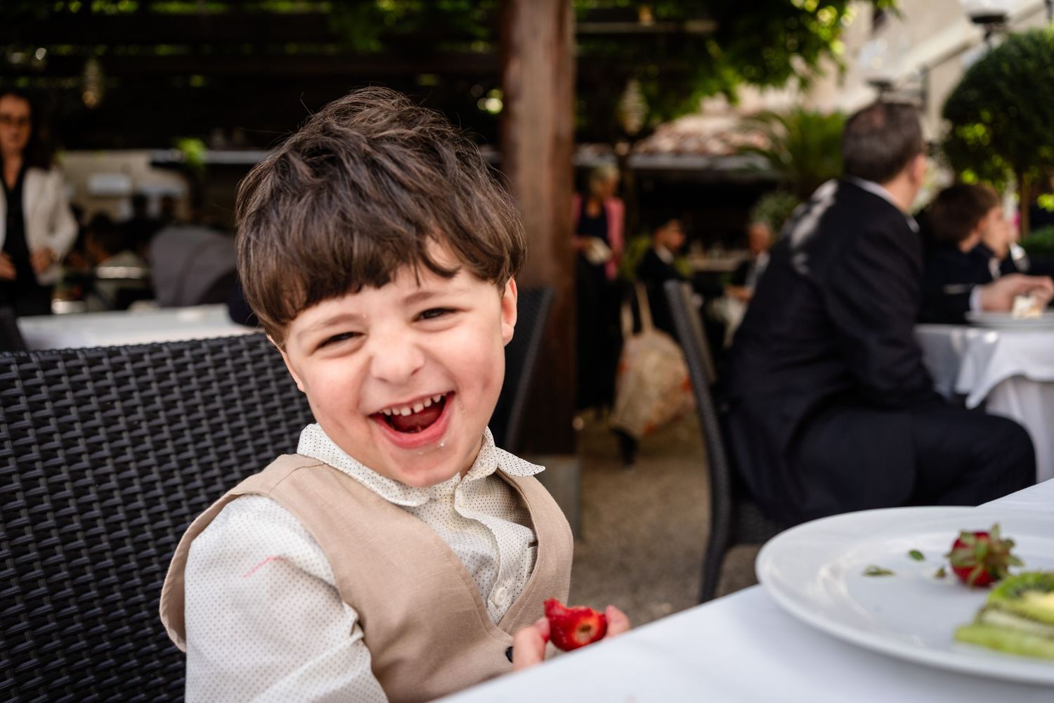 A person smiles while sitting at an outdoor dining table with a plate of food in front of them.