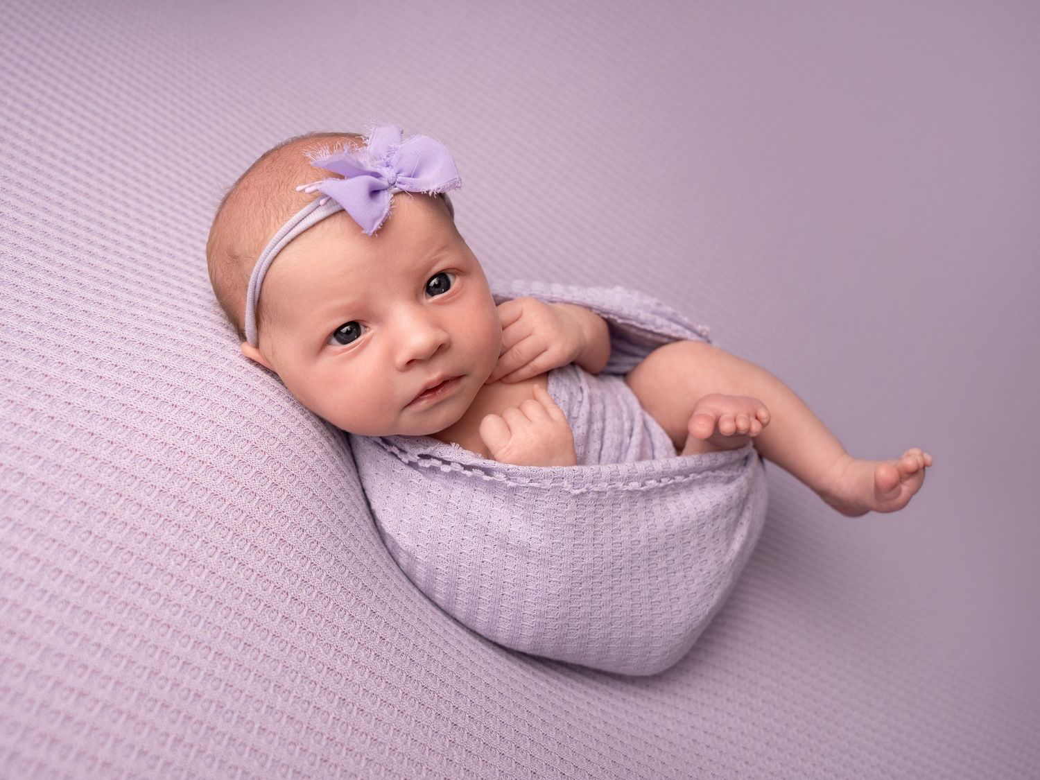 wide awake baby girl in purple bow wrapped in a blanket at photoshoot by newborn photographer in doncaster.