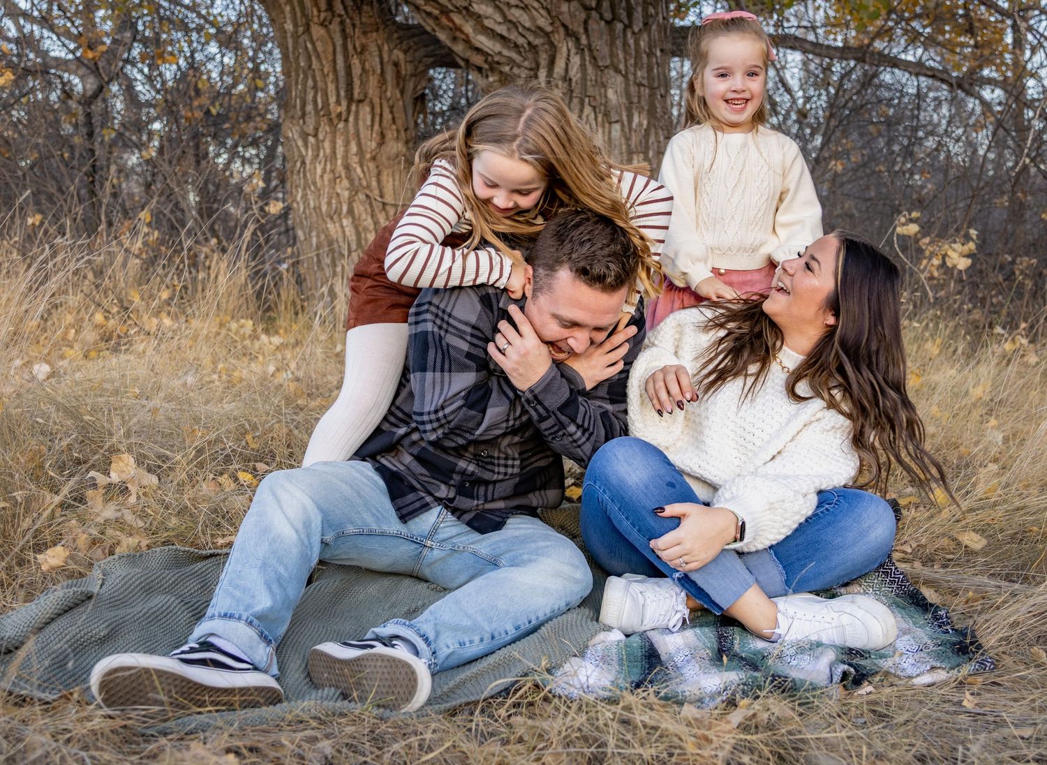 a couple with two young kids sitting on a blanket laughing.Family lifestyle session in Alberta by Creation Photography.