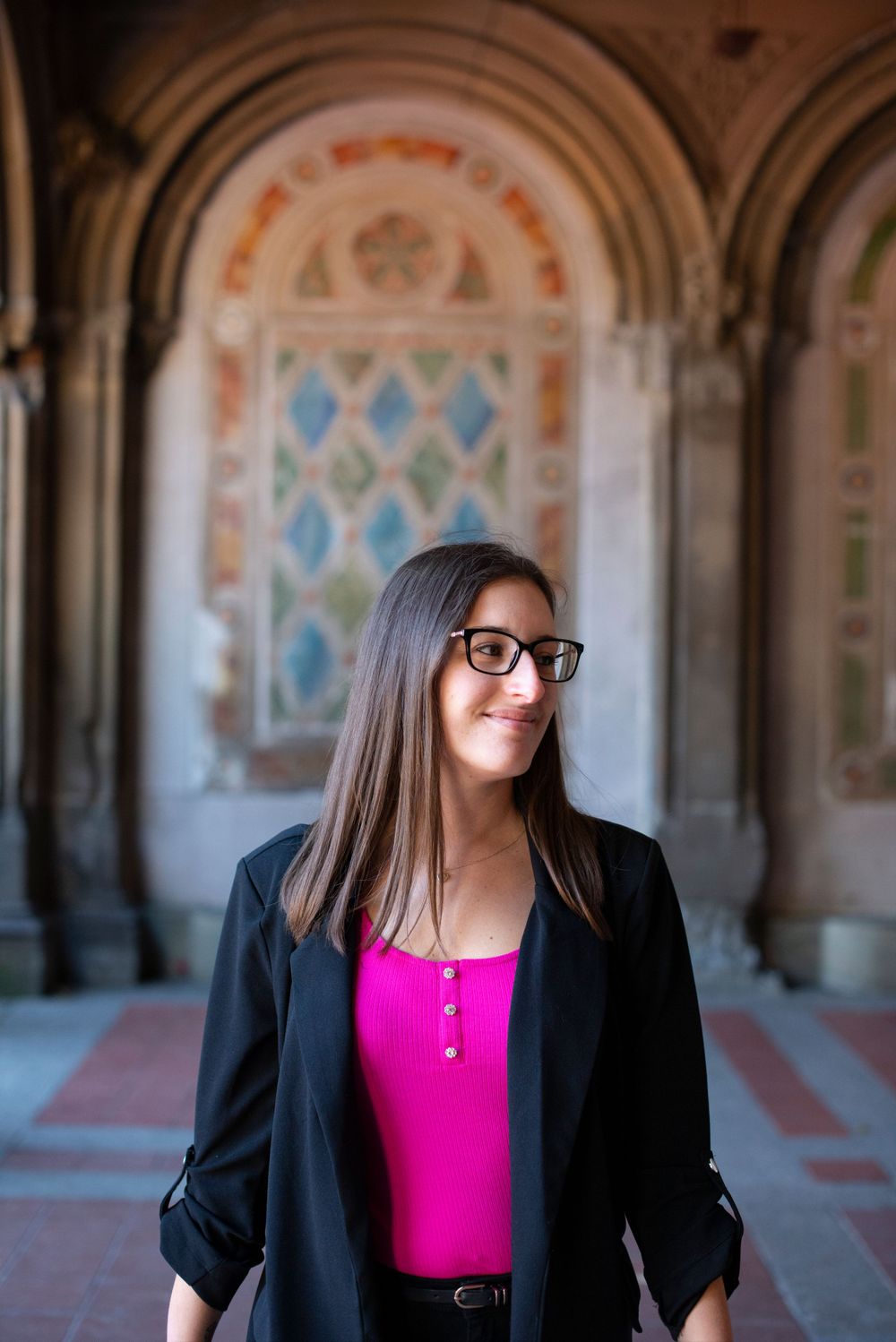 Woman in business attire stands under ornate archway with decorative tiles and patterns.