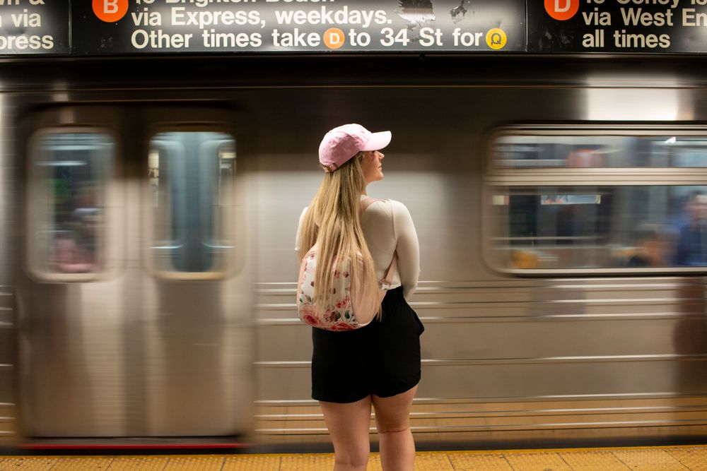 Person in pink hat waits for subway train at New York City station platform.