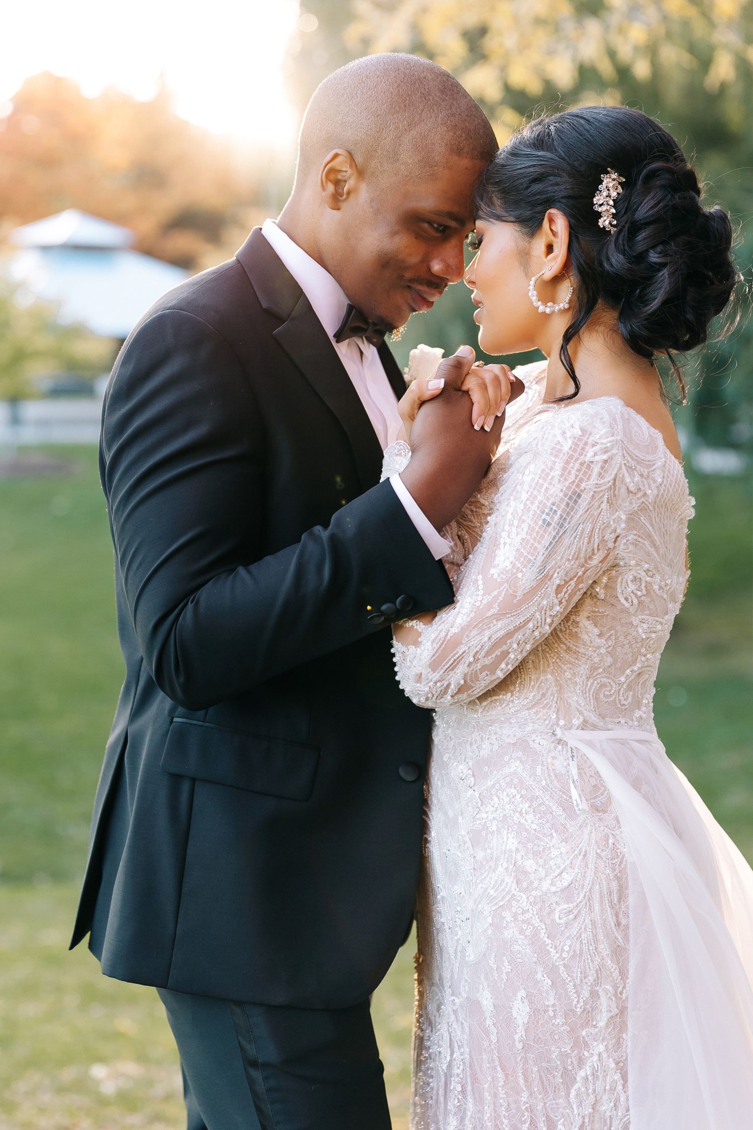 A tender wedding moment captured in golden sunset light showing a couple in formal attire sharing an intimate embrace outdoors.