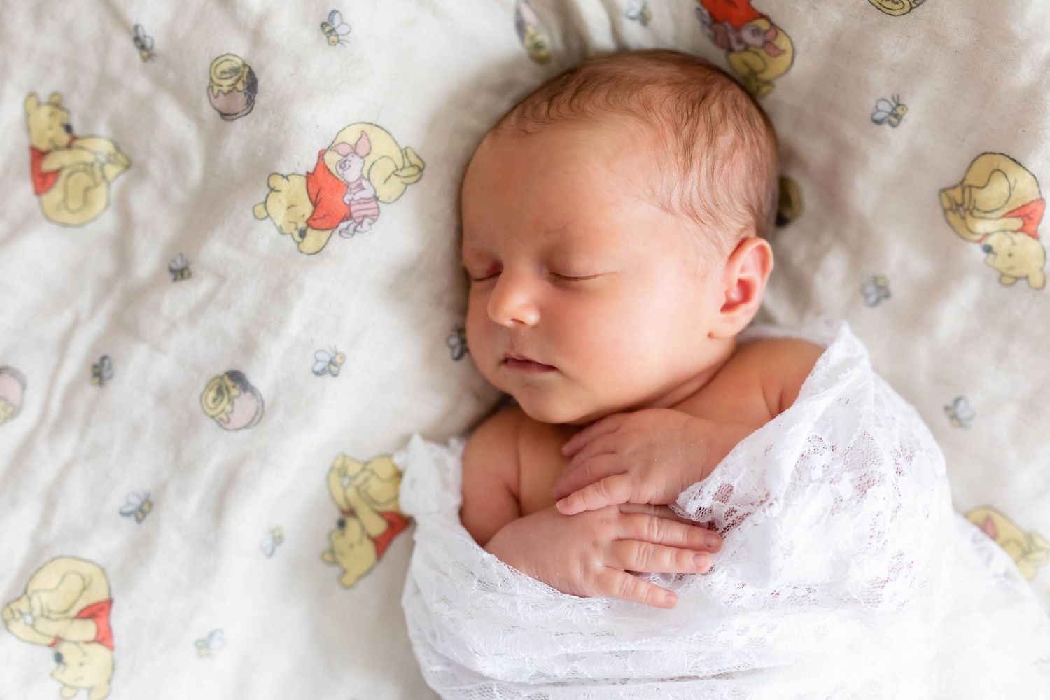 A sleeping newborn wrapped in white lace on a patterned blanket.